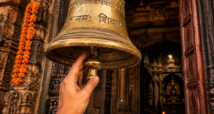 A close-up of a hand reaching to ring a heavy brass bell at the entrance of an ancient Indian temple, symbolizing the start of a spiritual journey.