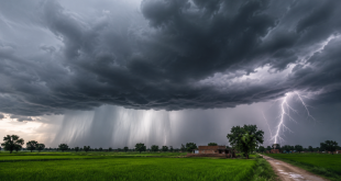A heavy monsoon cloud formation over a rural field in Uttar Pradesh, India, with visible distant rain curtains and lightning bolts.