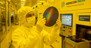 A modern cleanroom environment inside an Indian semiconductor fabrication facility showing an engineer in a white bunny suit handling a silicon wafer under specialized yellow lighting conditions.