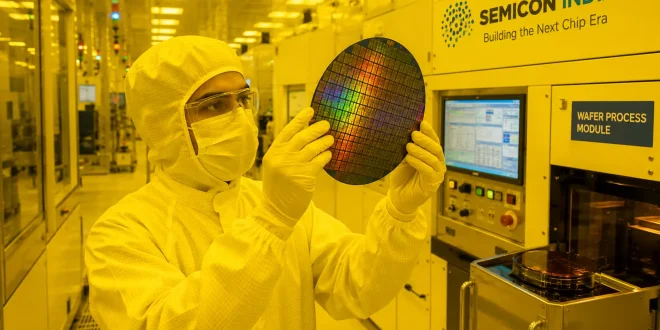 A modern cleanroom environment inside an Indian semiconductor fabrication facility showing an engineer in a white bunny suit handling a silicon wafer under specialized yellow lighting conditions.