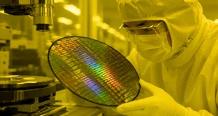 Close-up of an engineer inside a dust-free semiconductor cleanroom handling a silicon wafer under monochromatic light.