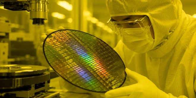 Close-up of an engineer inside a dust-free semiconductor cleanroom handling a silicon wafer under monochromatic light.