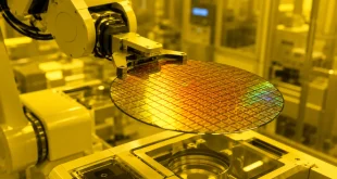 Close-up of a high-tech silicon wafer being handled by a robotic arm inside a dust-free, yellow-lit semiconductor fabrication cleanroom.