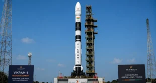 A sleek, seven-story-tall multi-stage Vikram-1 rocket by Skyroot Aerospace standing vertically on the launchpad at the Sriharikota spaceport under a clear sky.