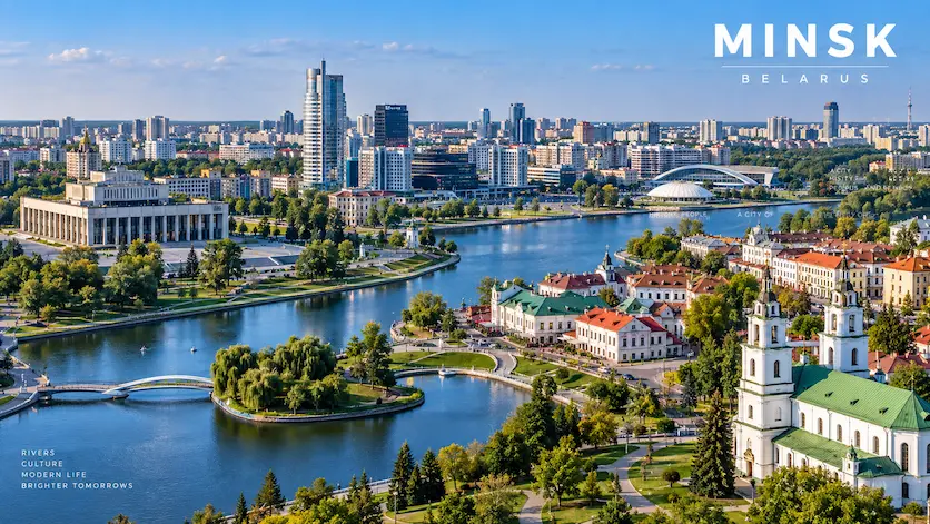 Aerial cityscape view of Minsk, Belarus featuring the Svislach River, urban architecture, and green spaces under a clear sky.